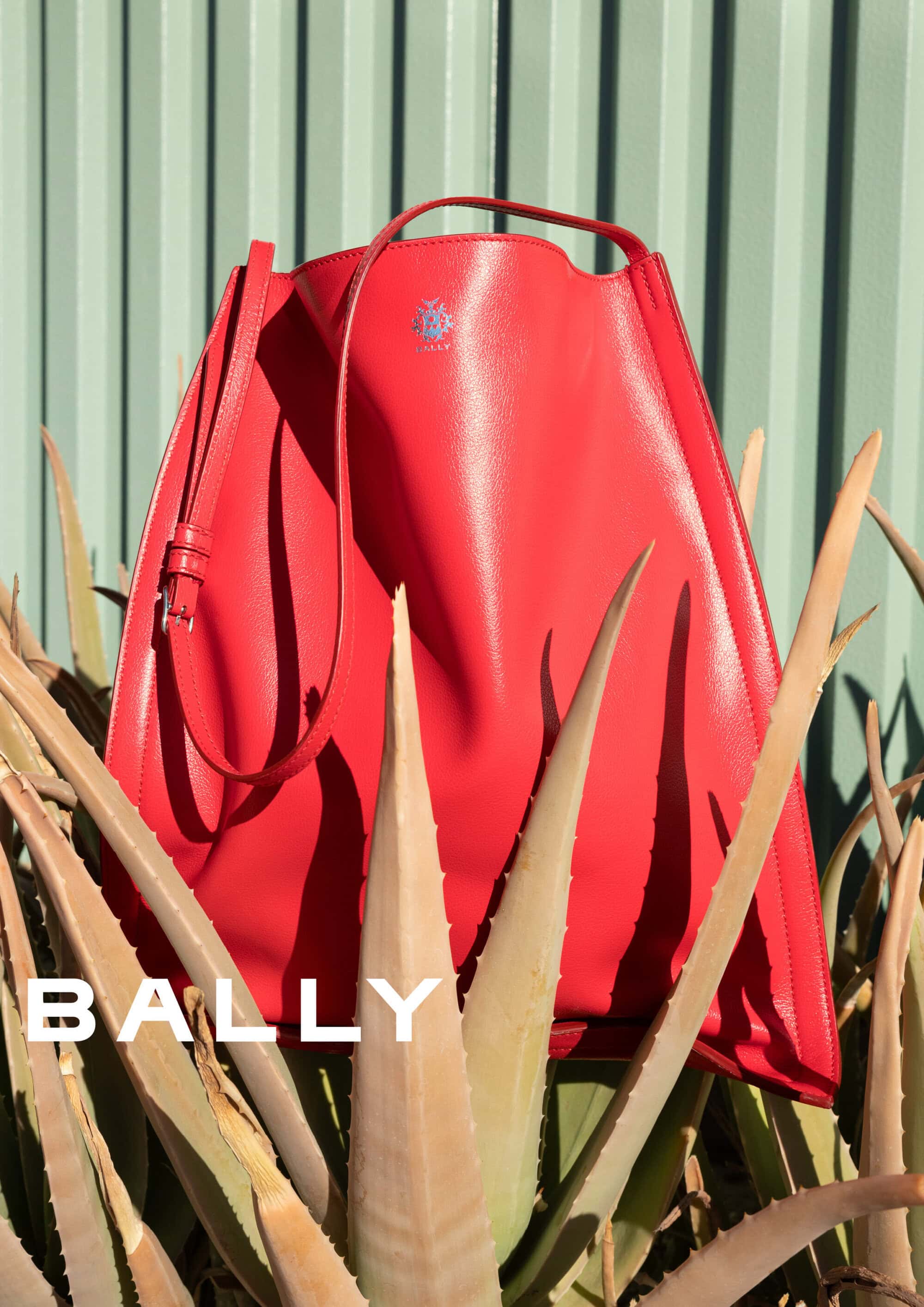 Bright red leather handbag nested amongst spiky green succulent leaves against a corrugated wall