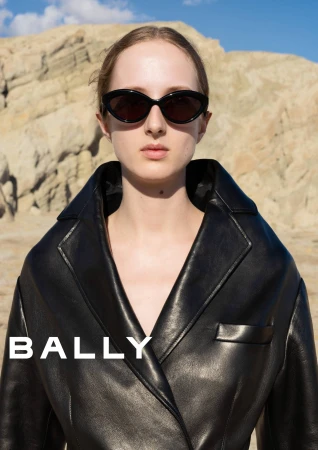 Model wearing black sunglasses and a dark leather coat outdoors against a rugged rock formation.