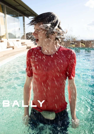 A man wearing a red mesh shirt standing in a swimming pool while water splashes across his face.