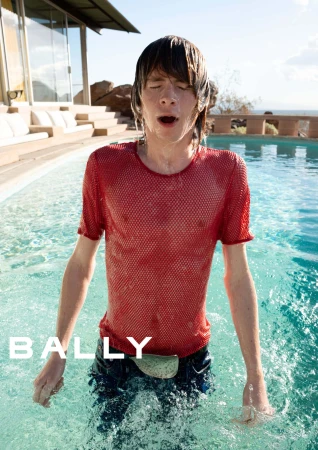 Wet man in a red mesh t-shirt standing in a swimming pool during the Bally Spring 2025 ad campaign photographed by Jack Pierson.