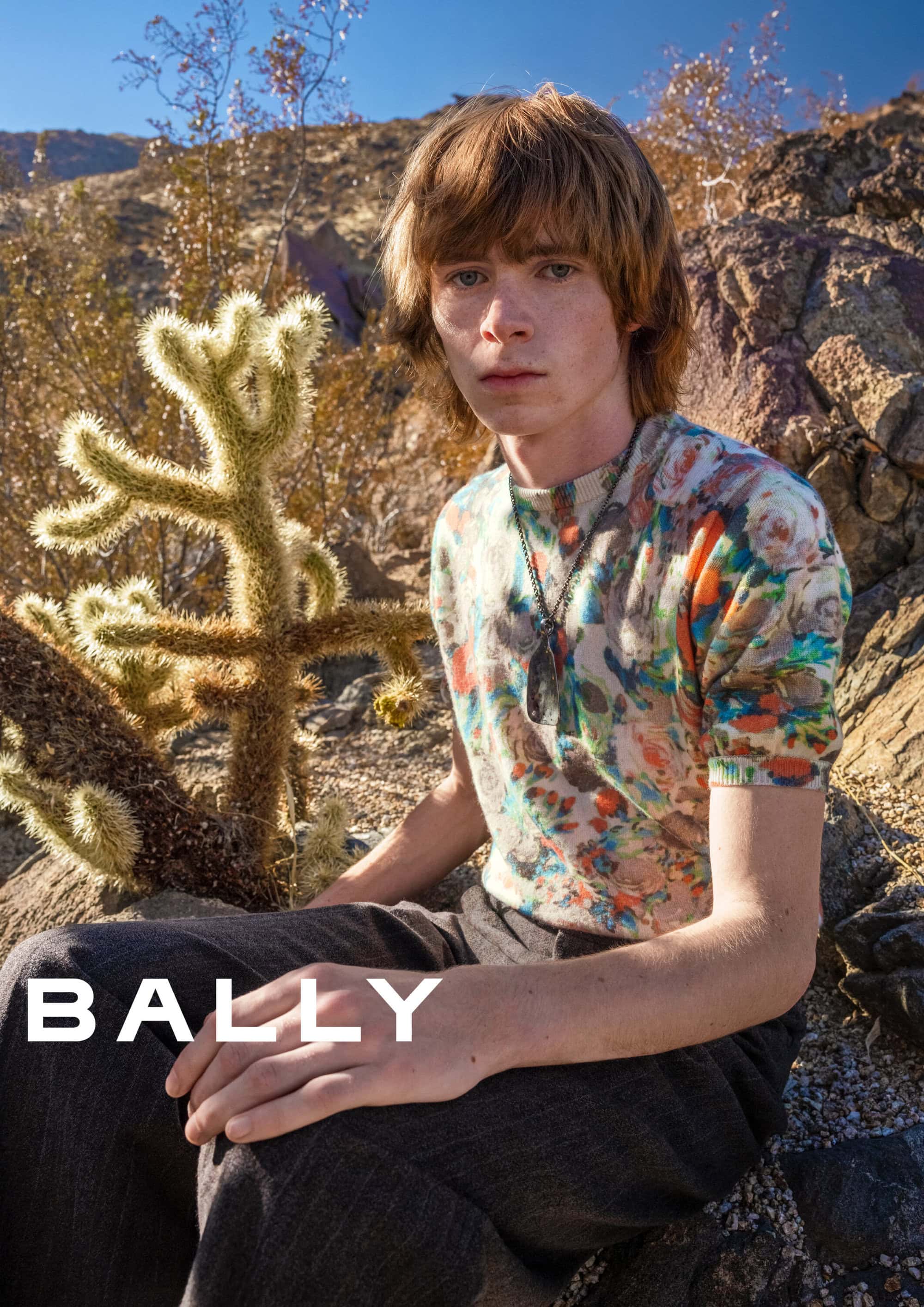 Model seated outdoors in an arid desert landscape next to a cactus wearing a floral patterned top