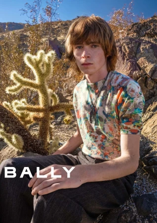 Model seated outdoors in an arid desert landscape next to a cactus wearing a floral patterned top