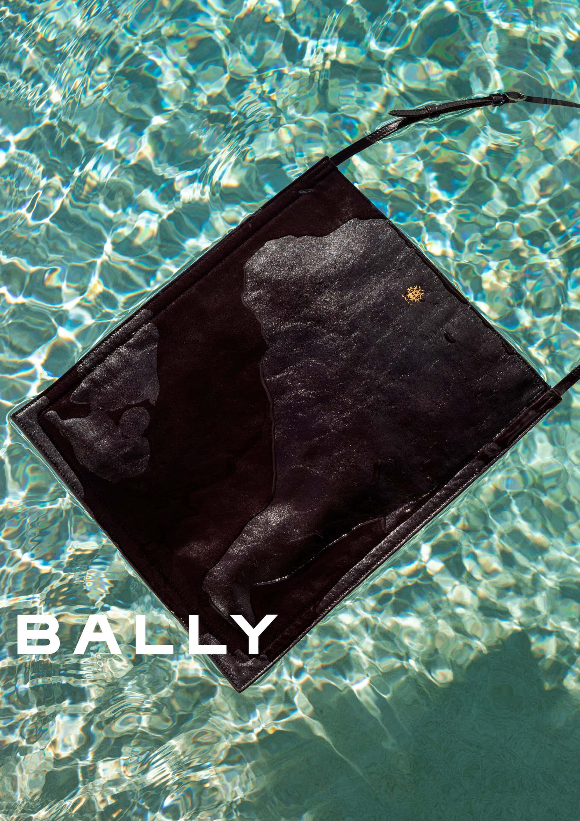 Dark leather shoulder bag floating in clear shimmering swimming pool water with visible Bally brand text