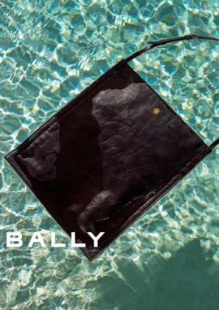 Dark leather shoulder bag floating in clear shimmering swimming pool water with visible Bally brand text