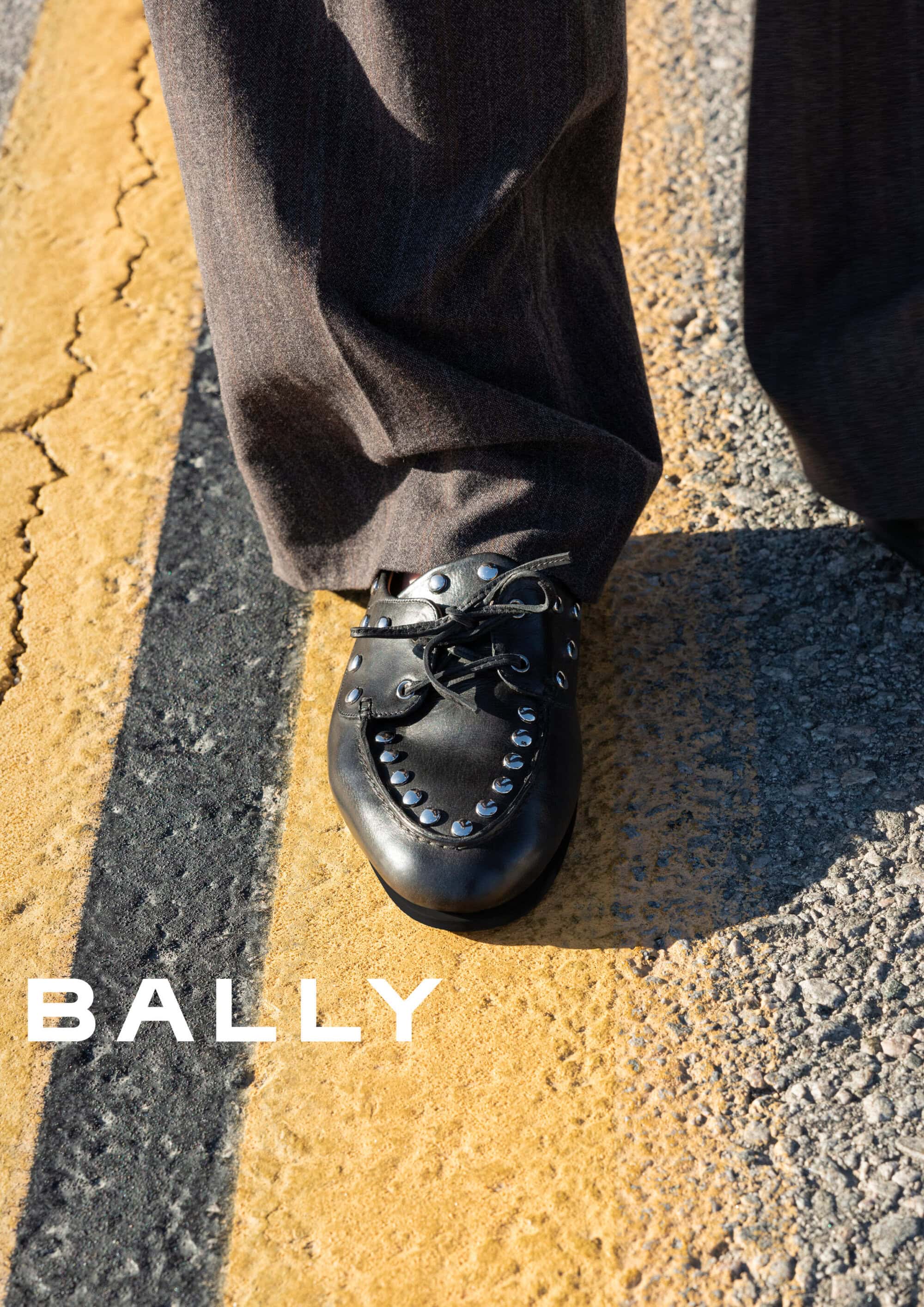 Close-up of black studded leather shoe on asphalt with yellow road markings for Bally spring ad campaign