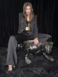 Laetitia Casta straddling a black panther sculpture wearing a black structured blazer and trousers for Balmain Spring 2025 ad campaign.