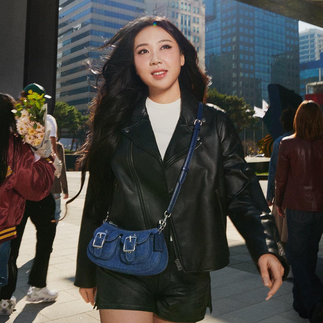 Youngji Lee wearing a black leather jacket and carrying a blue denim crossbody bag outdoors in an urban public square