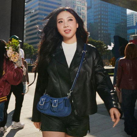 Youngji Lee wearing a black leather jacket and carrying a blue denim crossbody bag outdoors in an urban public square