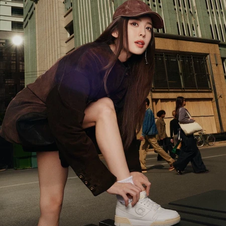 Nazha wearing a brown cap and jacket tying her white sneaker on a city street for Coach ad campaign