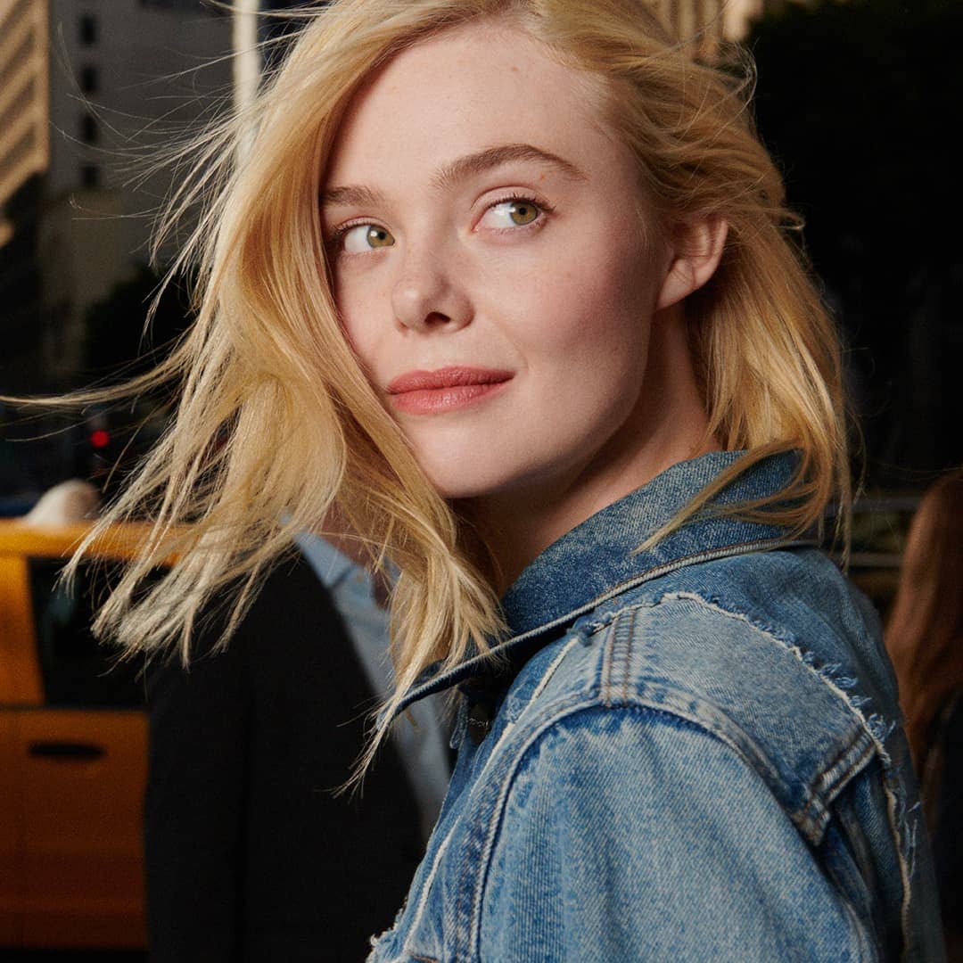 Elle Fanning wearing a denim jacket on an outdoor city street for the Coach Spring 2025 ad campaign.