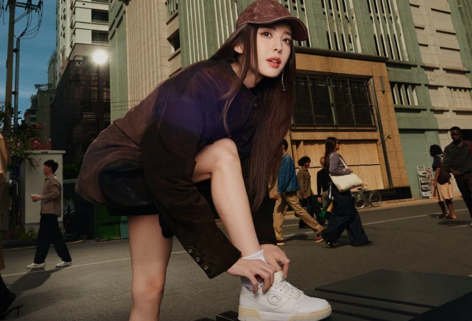 Nazha wearing a brown cap and jacket tying her white sneakers on a city street for Coach Spring 2025 campaign