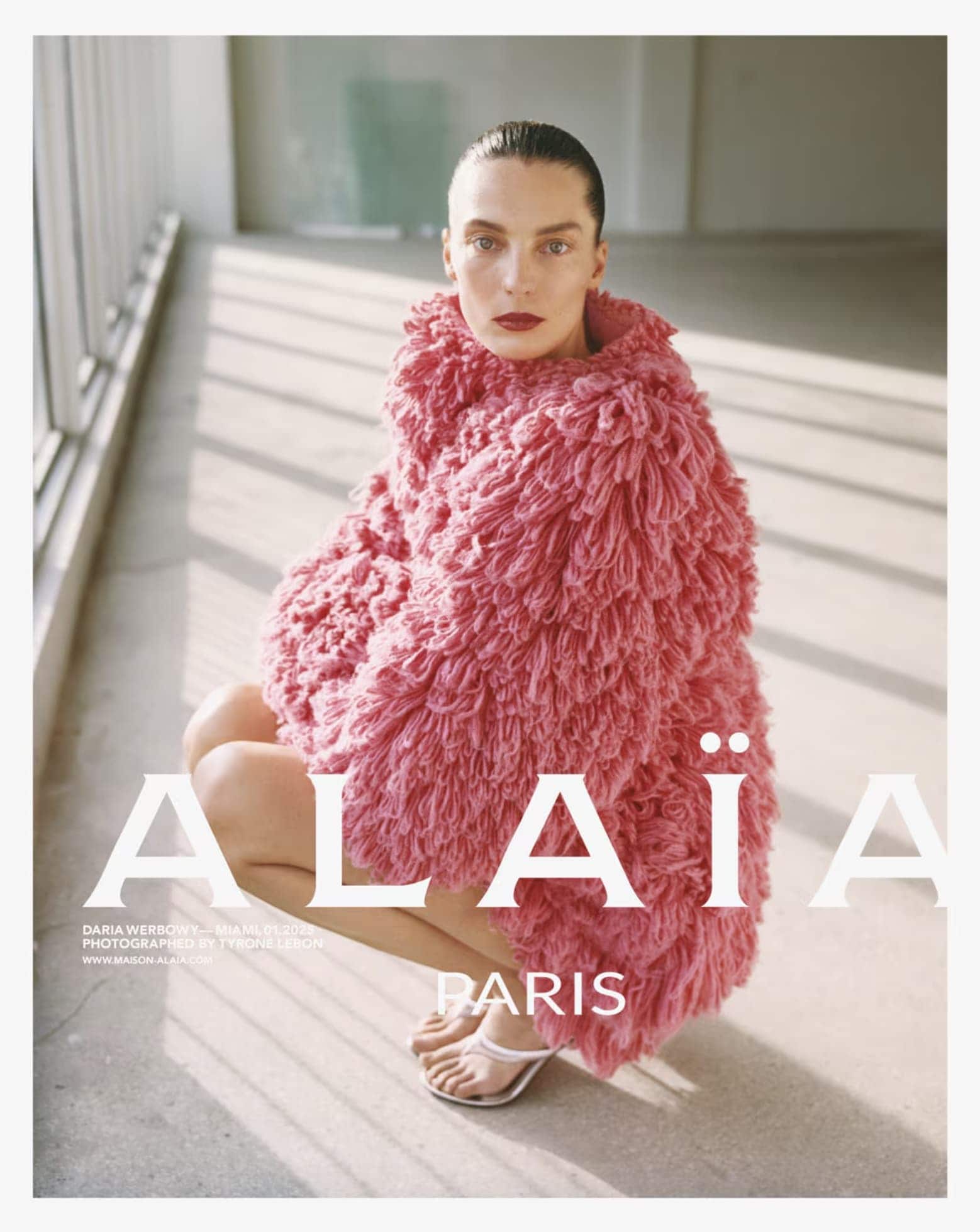 Model Daria Werbowy in a textured pink coat squatting in an interior space for Alaïa Spring 2025 campaign.