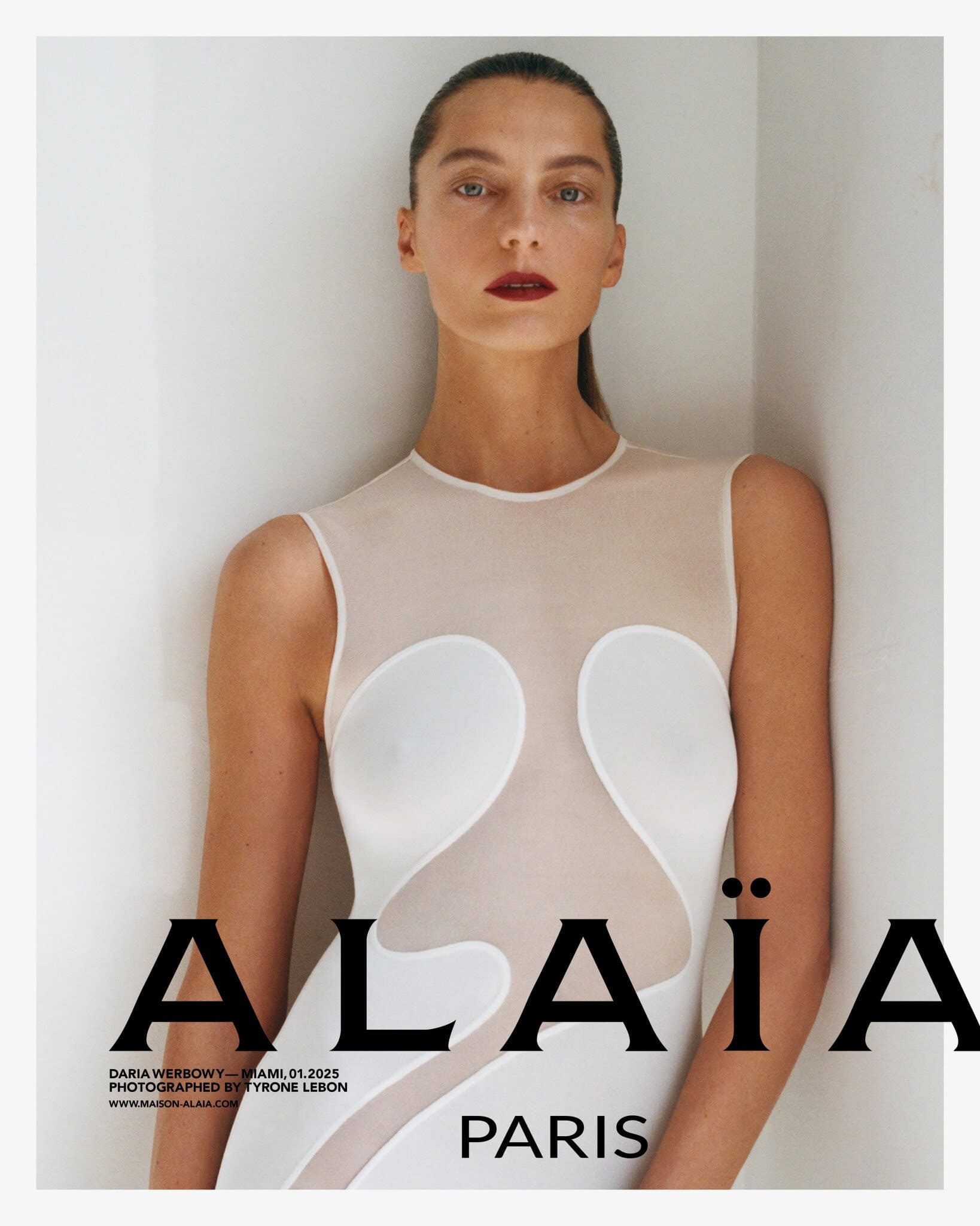 Model Daria Werbowy posing against a plain white wall wearing a form-fitting white dress for Alaïa