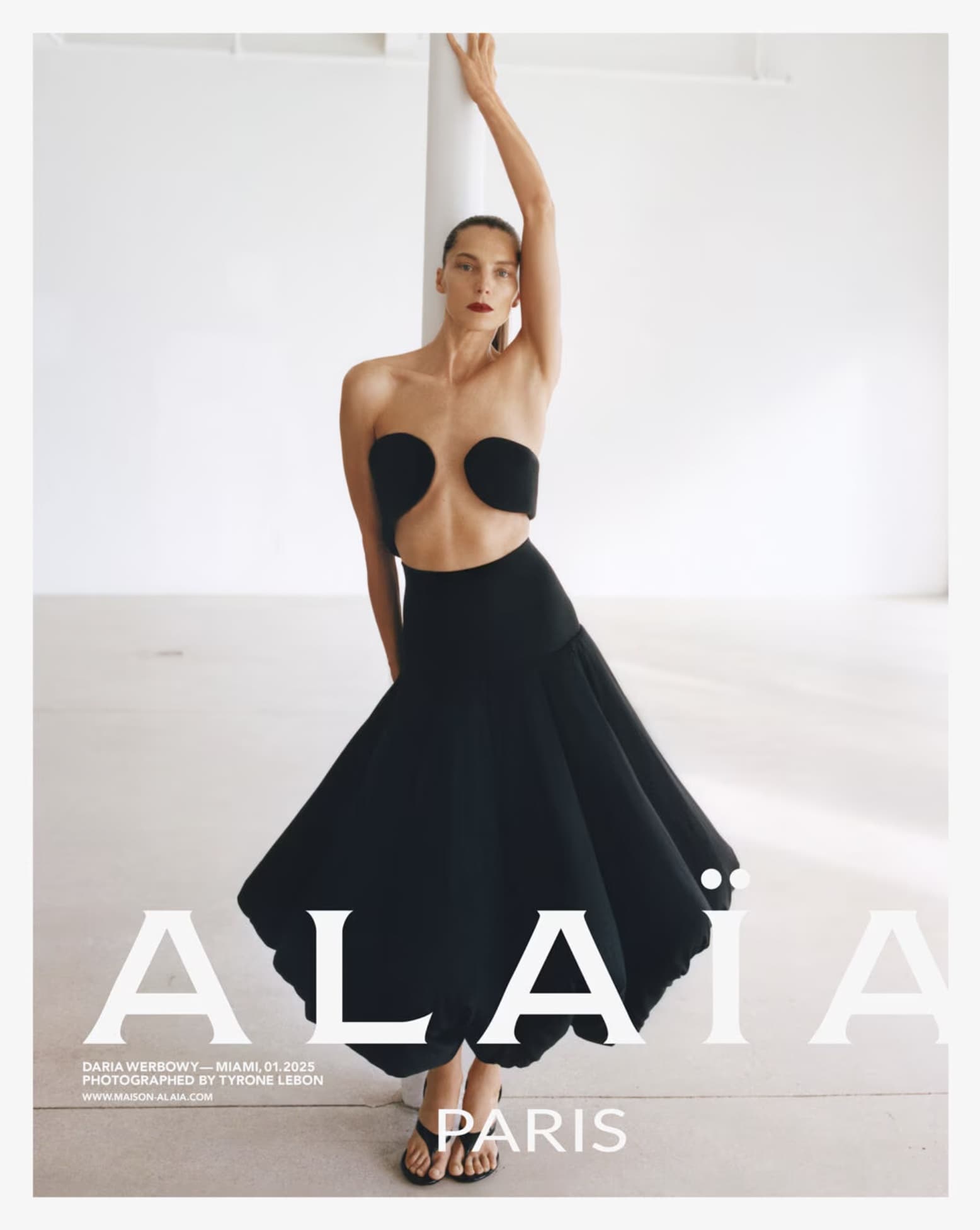 Model Daria Werbowy posing in a black sculptural dress against a white seamless background for the Alaïa Spring 2025 campaign.