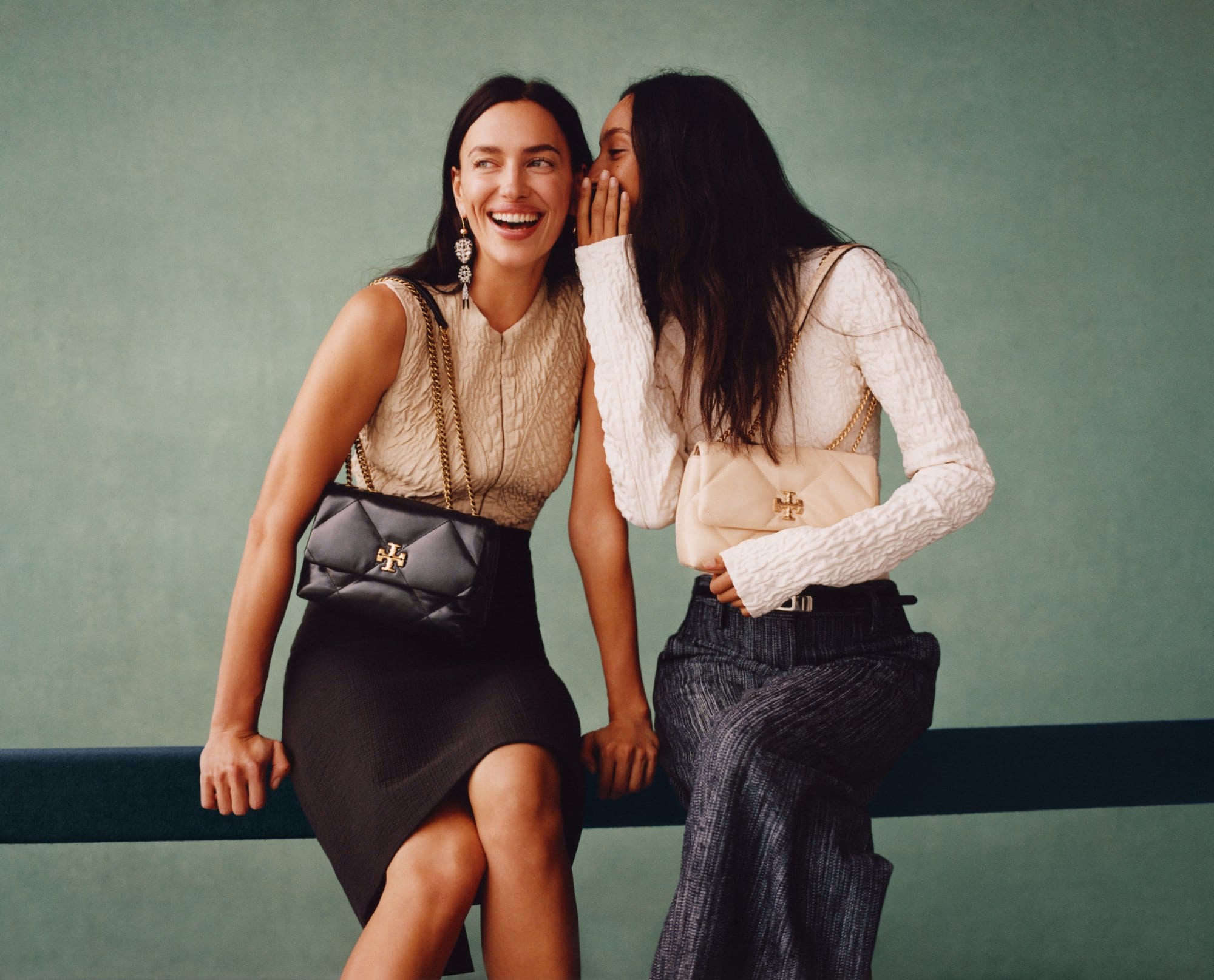 Models Irina Shayk and Mona Tougaard laughing together with quilted shoulder bags for Tory Burch