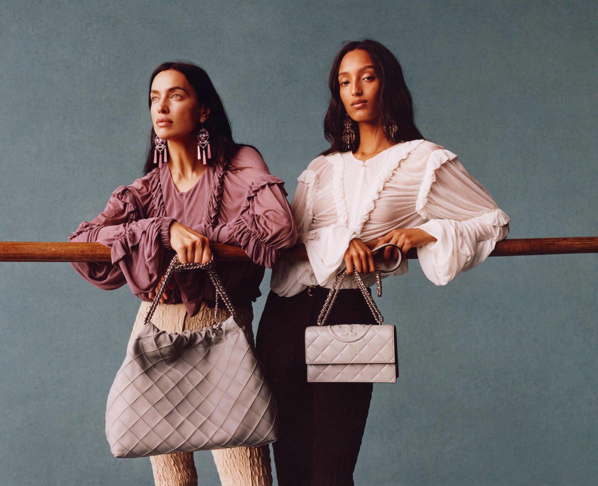 Two female models leaning against a wooden bar holding luxury handbags for Tory Burch Spring 2025 ad campaign