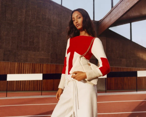 Model Mona Tougaard wearing a red and white sweater holding a white bag on a sports track