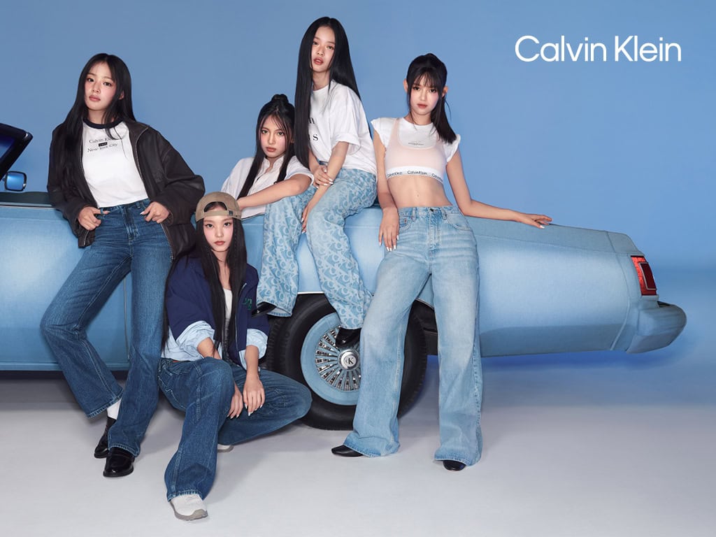 Five models posing with a vintage blue car against a clean studio backdrop for the Calvin Klein spring 2025 ad campaign.