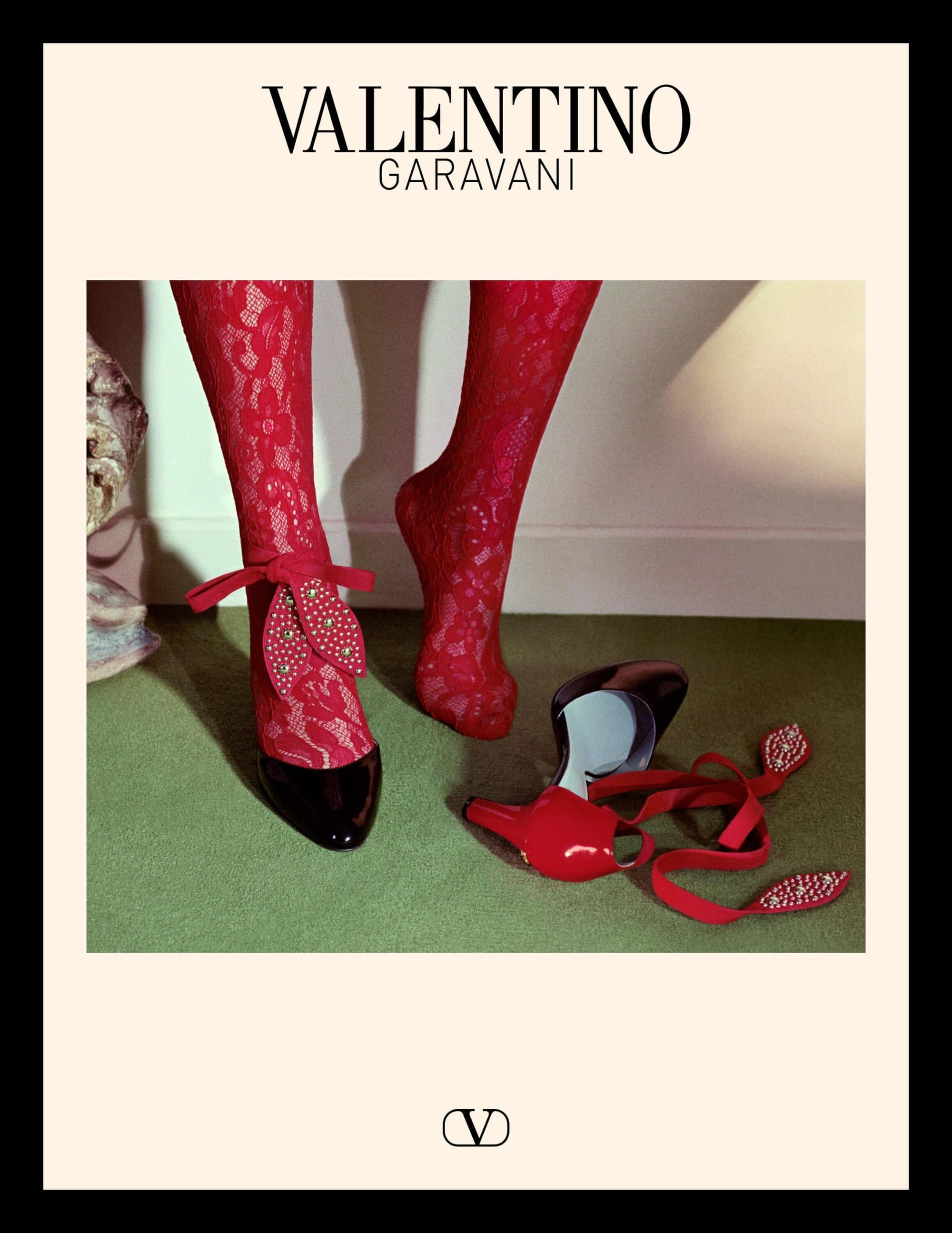 Close-up of legs wearing red lace stockings and heels next to a red shoe on a green carpet for Valentino Spring 2025 ad campaign.