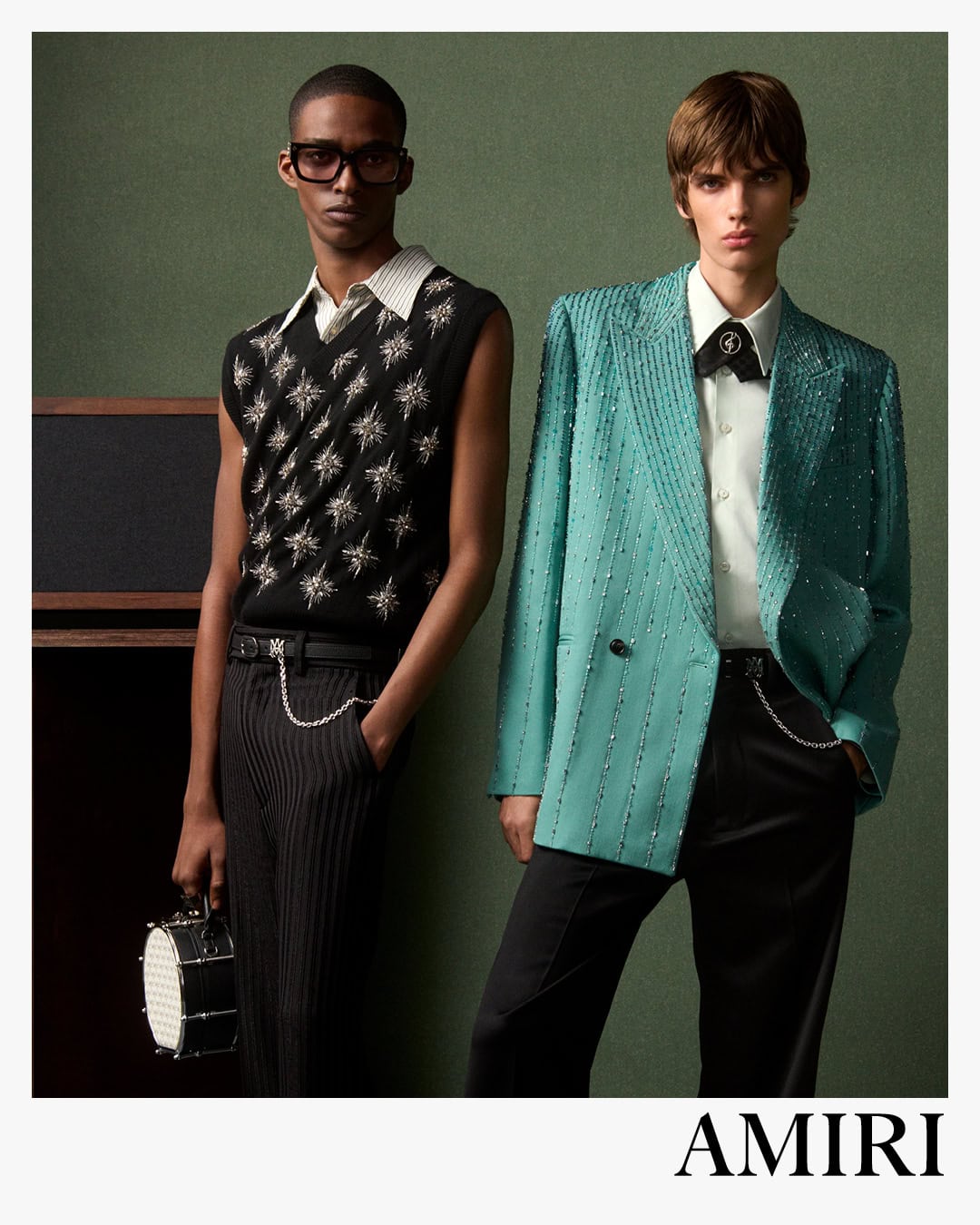 Two male models posing against a textured green background for Amiri spring 2025 ad campaign, photographed by Drew Vickers.