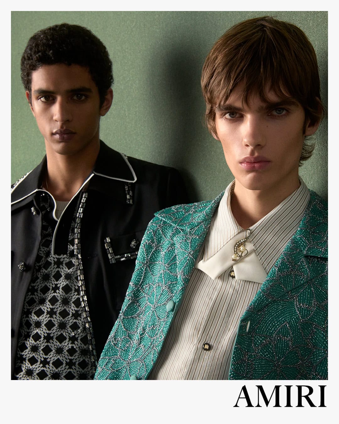 Two male models posing against a textured green wall for the Amiri Spring 2025 ad campaign, photographed by Drew Vickers