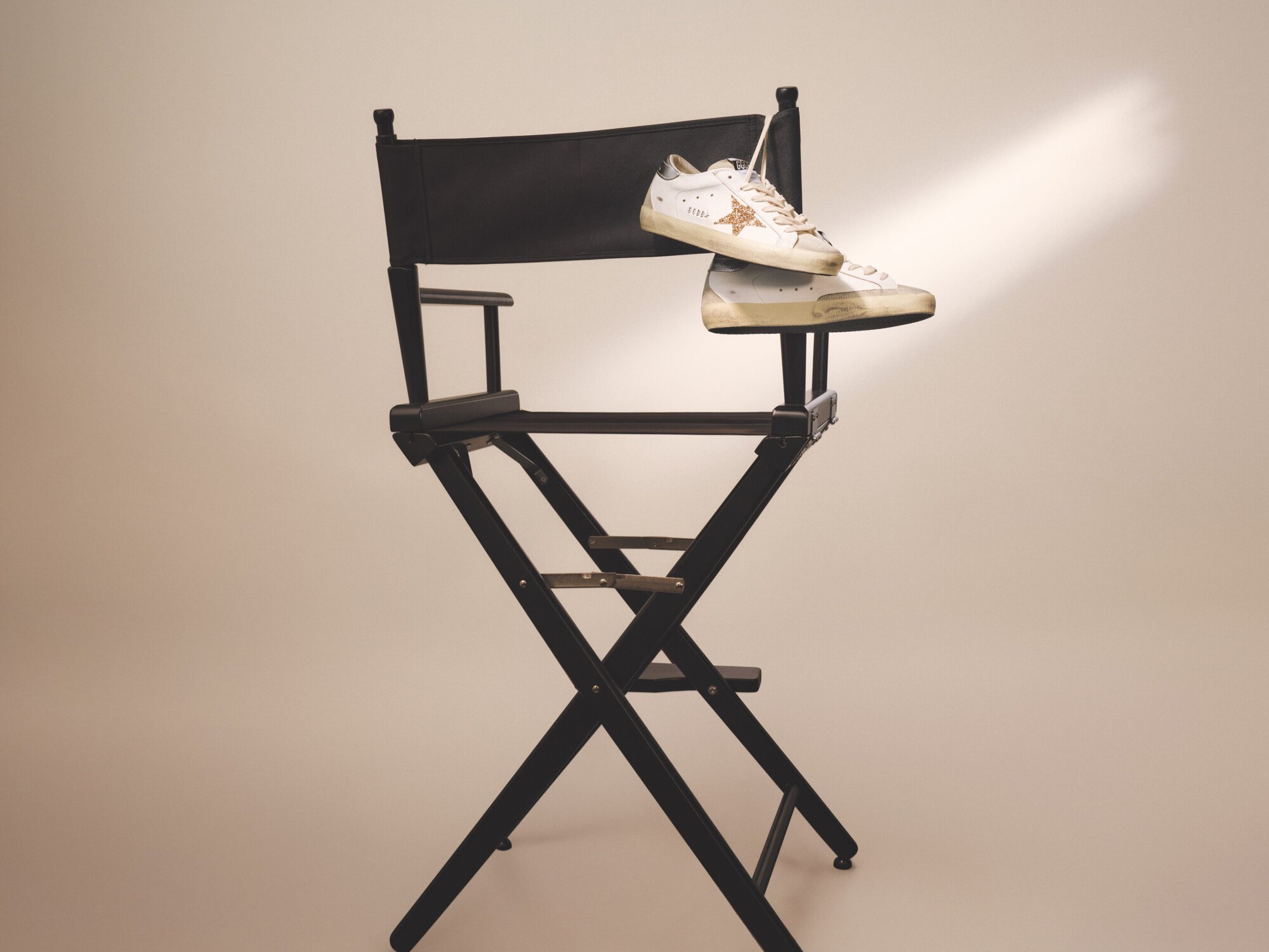 A pair of distressed white sneakers resting on a black director's chair against a neutral studio backdrop with soft light.