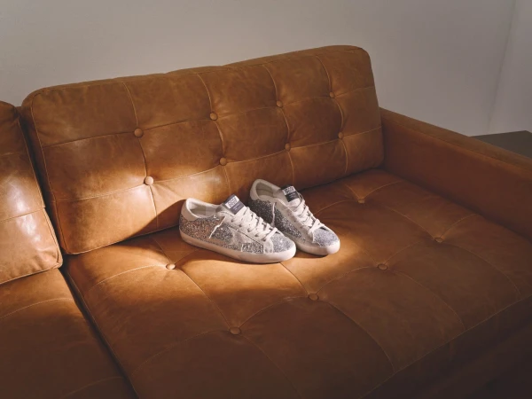 A pair of glitter sneakers resting on a brown tufted leather sofa under warm ambient lighting.