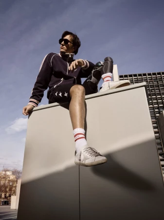 Man wearing sunglasses and athletic wear sitting atop a concrete structure against a blue sky