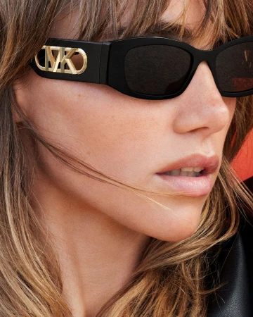 Close-up portrait of a woman wearing black sunglasses with gold hardware on the temple, shot by Mert Alas for Michael Kors.