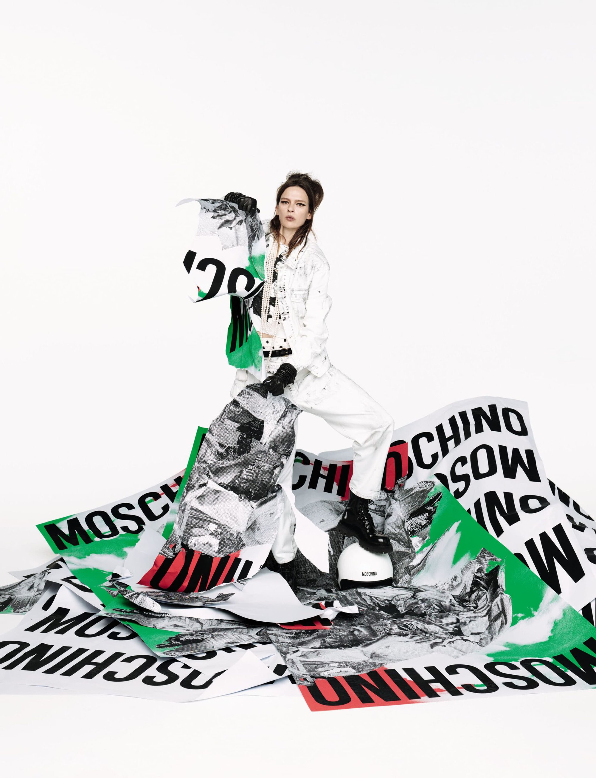 Model standing among large printed posters on white background for Moschino