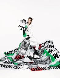 Model standing among large printed posters on white background for Moschino