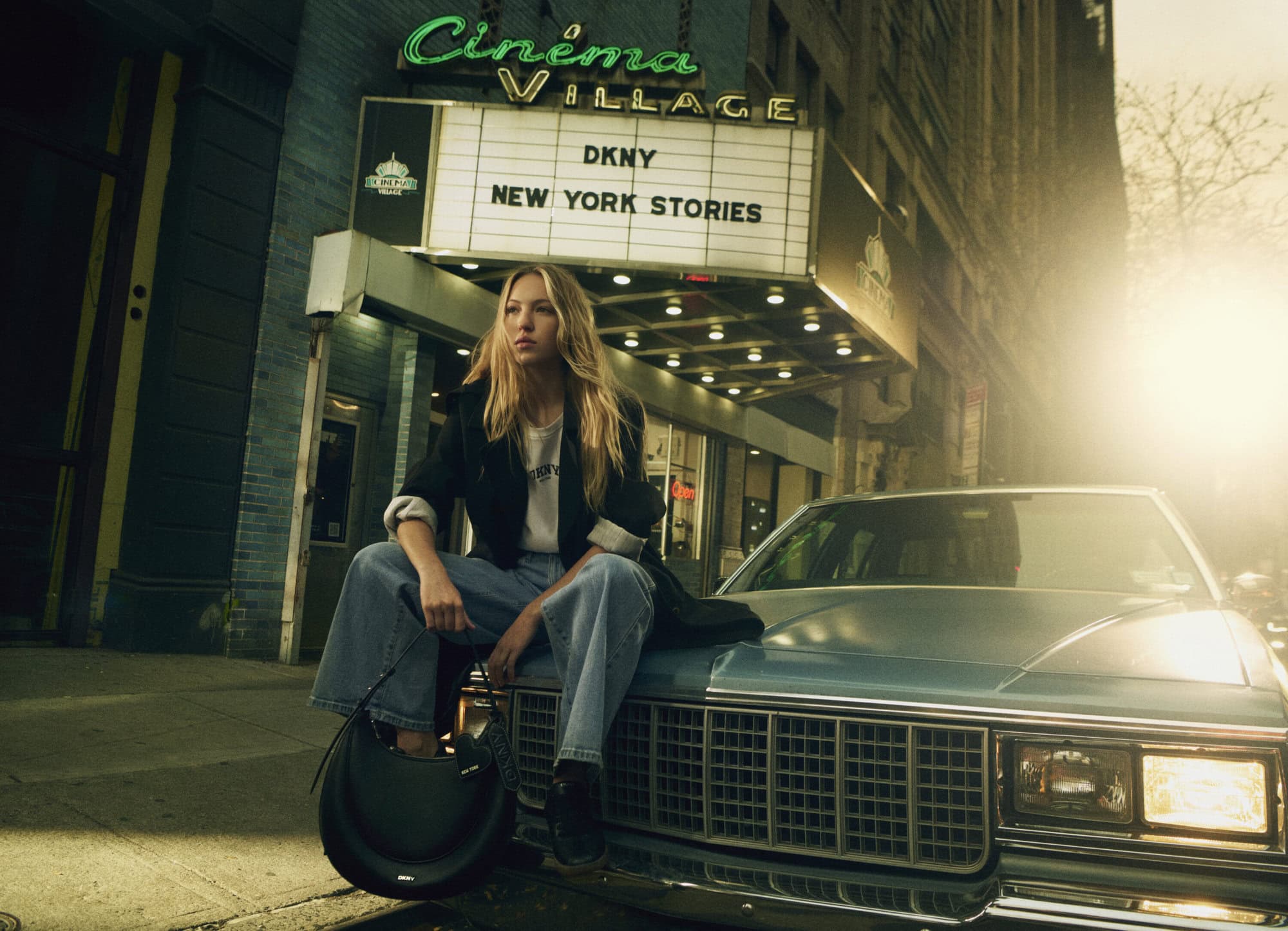 Model Lila Moss sitting on the hood of a vintage car outside Cinema Village for DKNY Spring 2025 ad campaign.