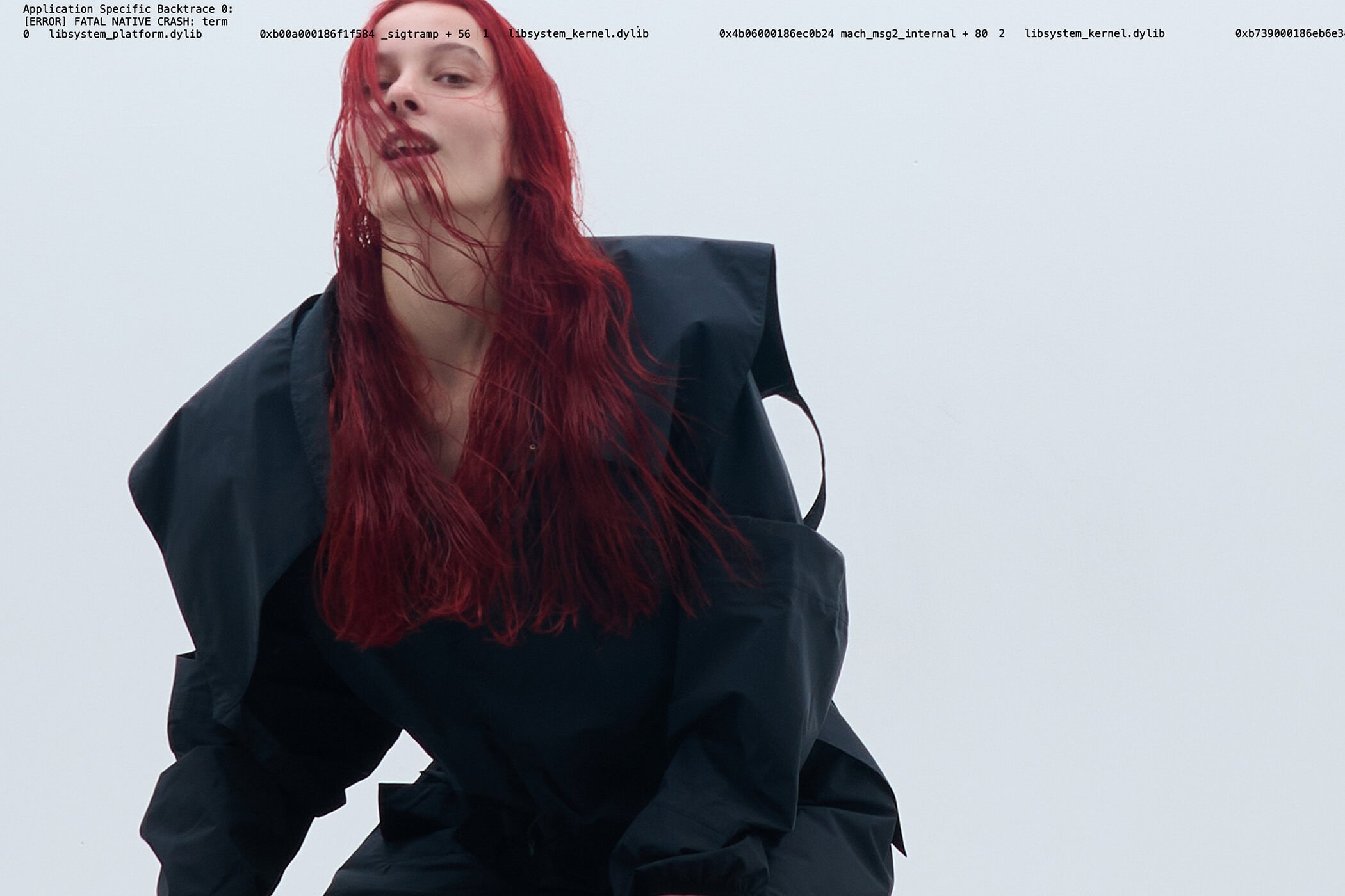 Woman with long red hair wearing a dark utility jacket against a plain light background with printed telemetry text.
