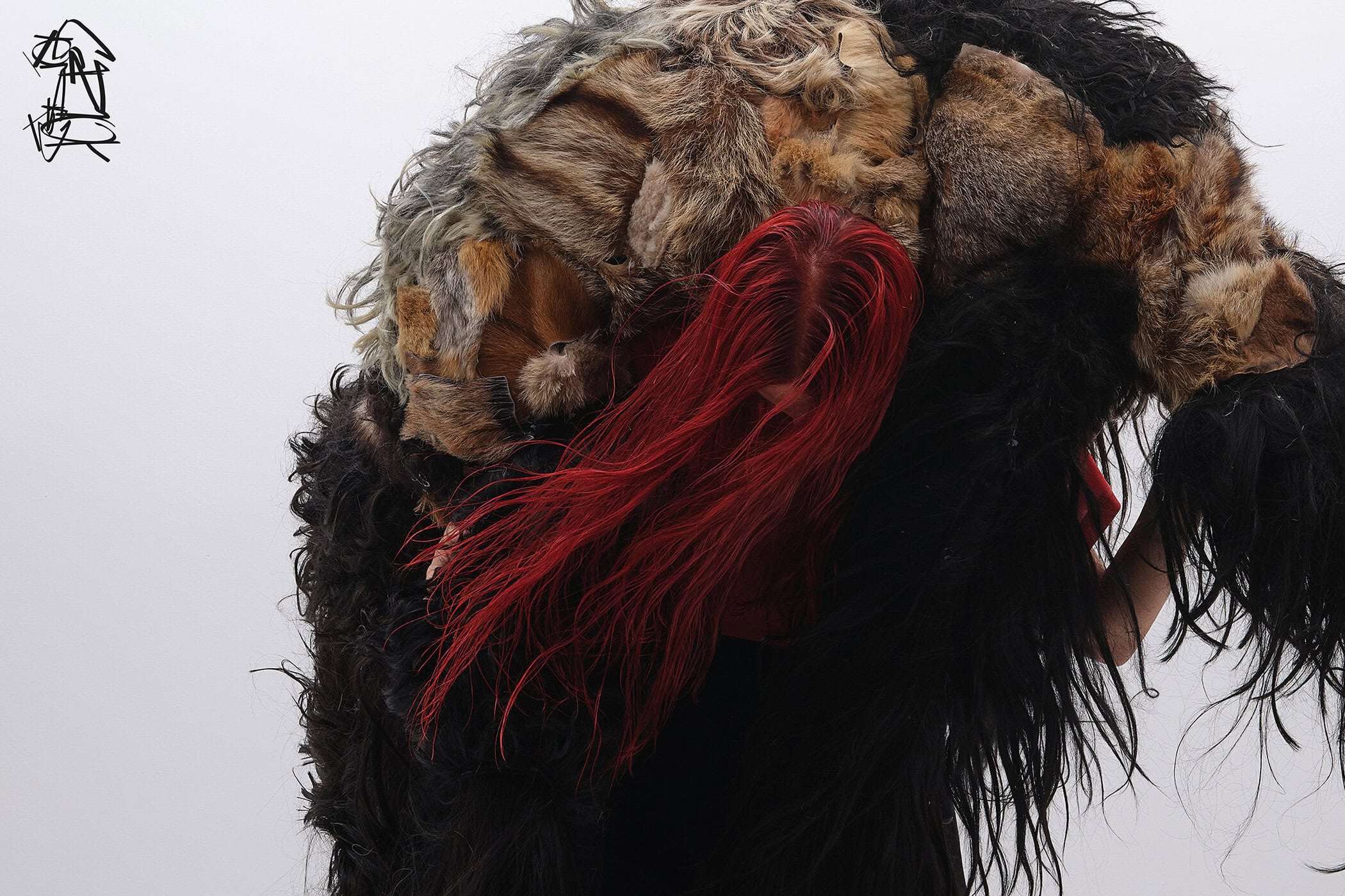 Model with vibrant red hair wearing heavy textured fur and black apparel against a seamless white background.