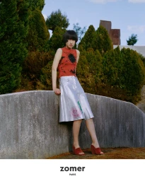 Model in a red patterned top and metallic skirt leaning against a concrete wall outdoors in Japan