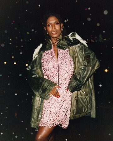 Model Jodie Turner Smith wearing a green jacket over a pink dress against a dark nighttime street background.
