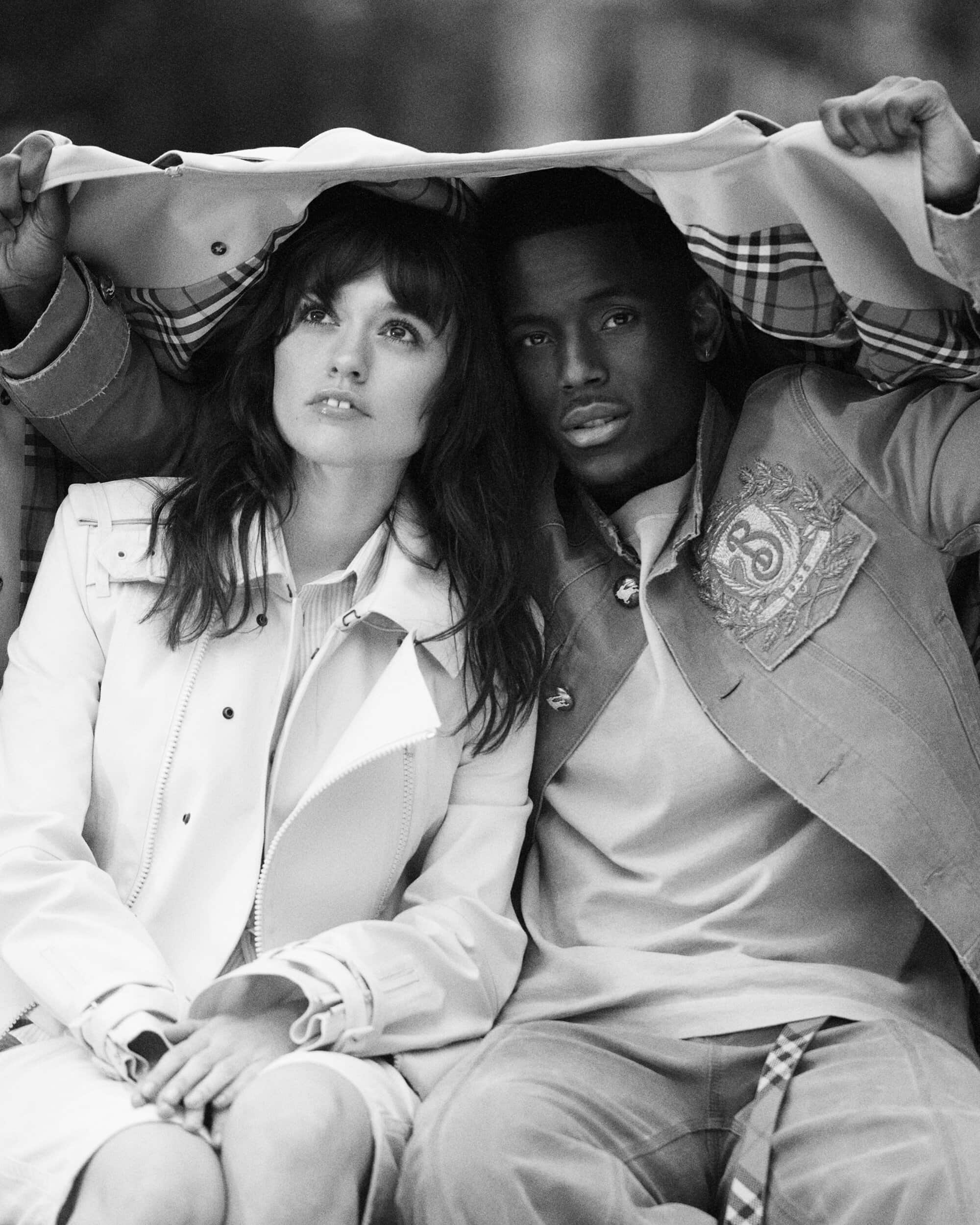Black and white portrait of a woman and man huddled underneath a trench coat held overhead, captured by Drew Vickers for Burberry.