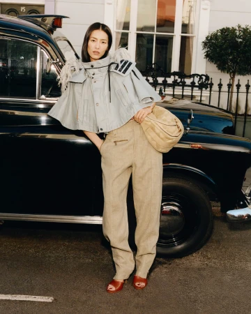 Model Liu Wen leaning against a vintage black car wearing a light grey cape and tan trousers in London