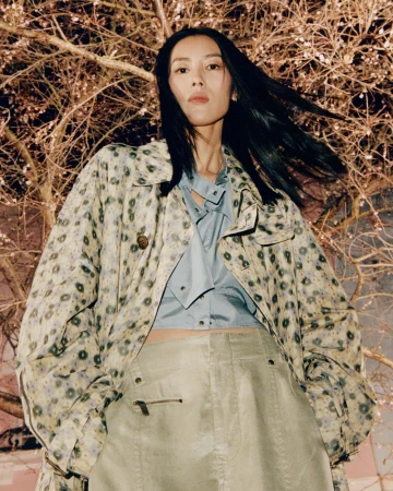 Model Liu Wen in patterned trench coat and blue shirt against bare branches in London for Burberry 2025 campaign.