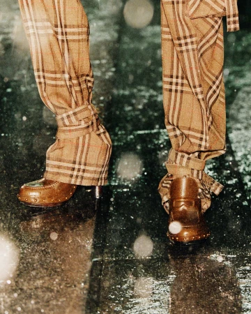 Close-up of trousers in iconic check pattern paired with brown loafers standing on wet pavement