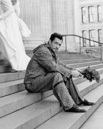 David Gandy wearing a plaid suit holding roses sitting on stone steps outside a building in London