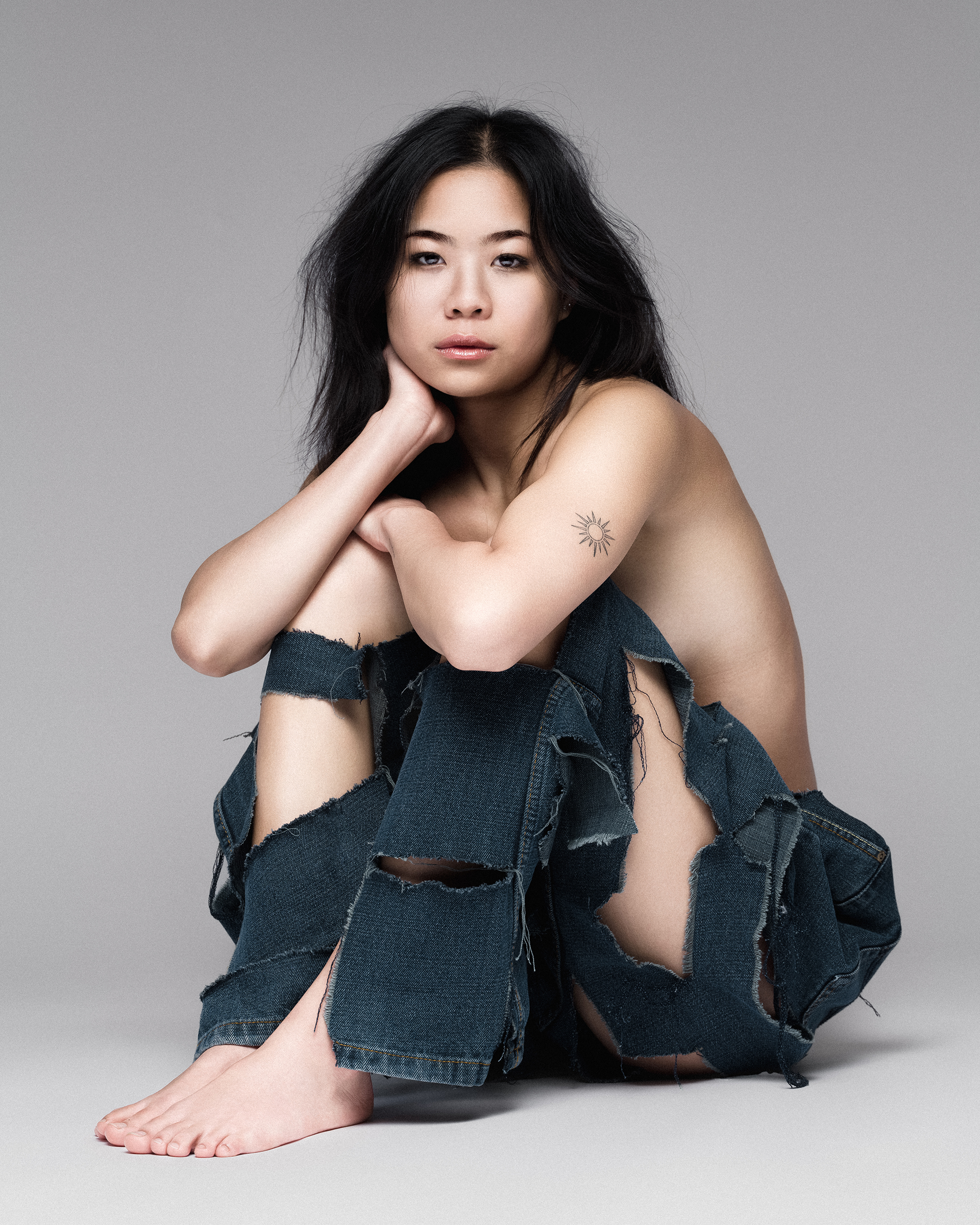 Model Joyce Lee seated wearing distressed dark denim jeans against a seamless grey backdrop, photographed by Juan Santamaria