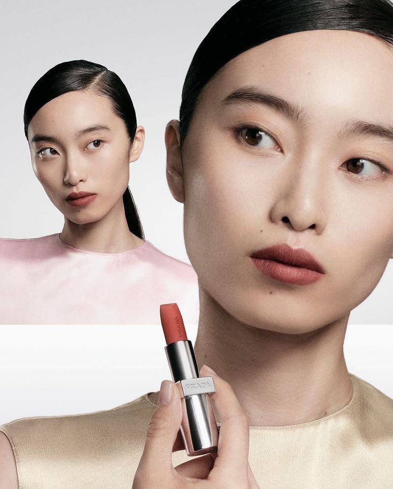 Close-up beauty shot featuring two Asian female models with sleek hairstyles, demonstrating a coral lipstick product in a studio setting.