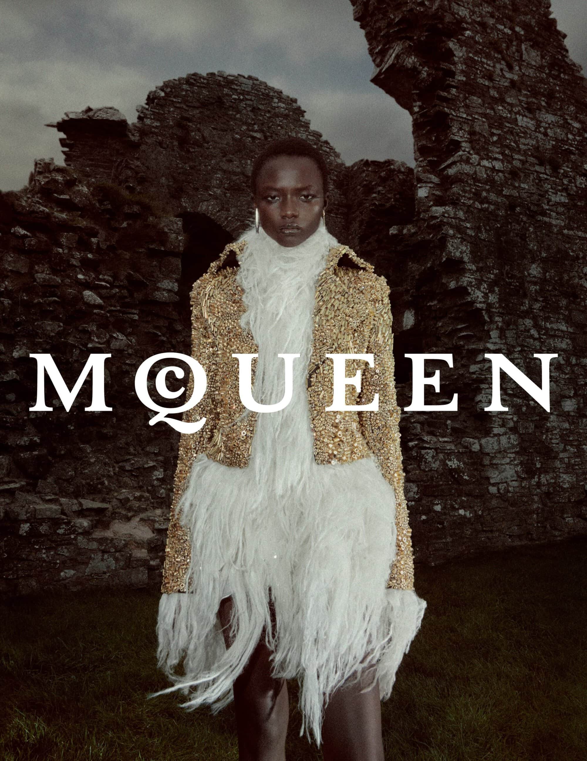 Model standing outdoors in front of stone ruins wearing a textured gold jacket and white feather scarf.