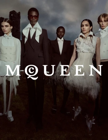Five models in tailored suits and dresses posing outdoors under an overcast sky for McQueen Spring 2025 campaign.
