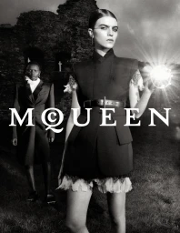 Black and white fashion campaign image featuring two models standing outdoors before a ruined stone building holding a glowing light source.