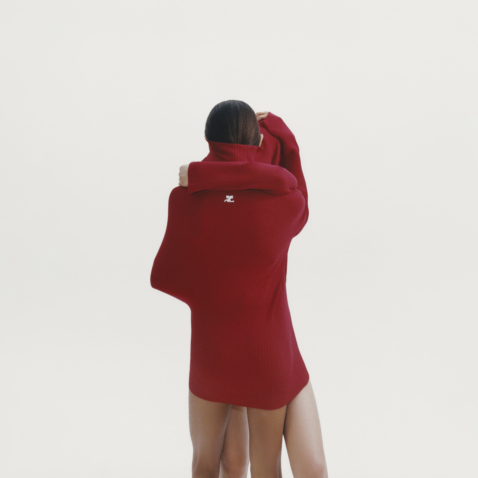 Two people embracing while wearing an oversized red turtleneck sweater against a plain white background