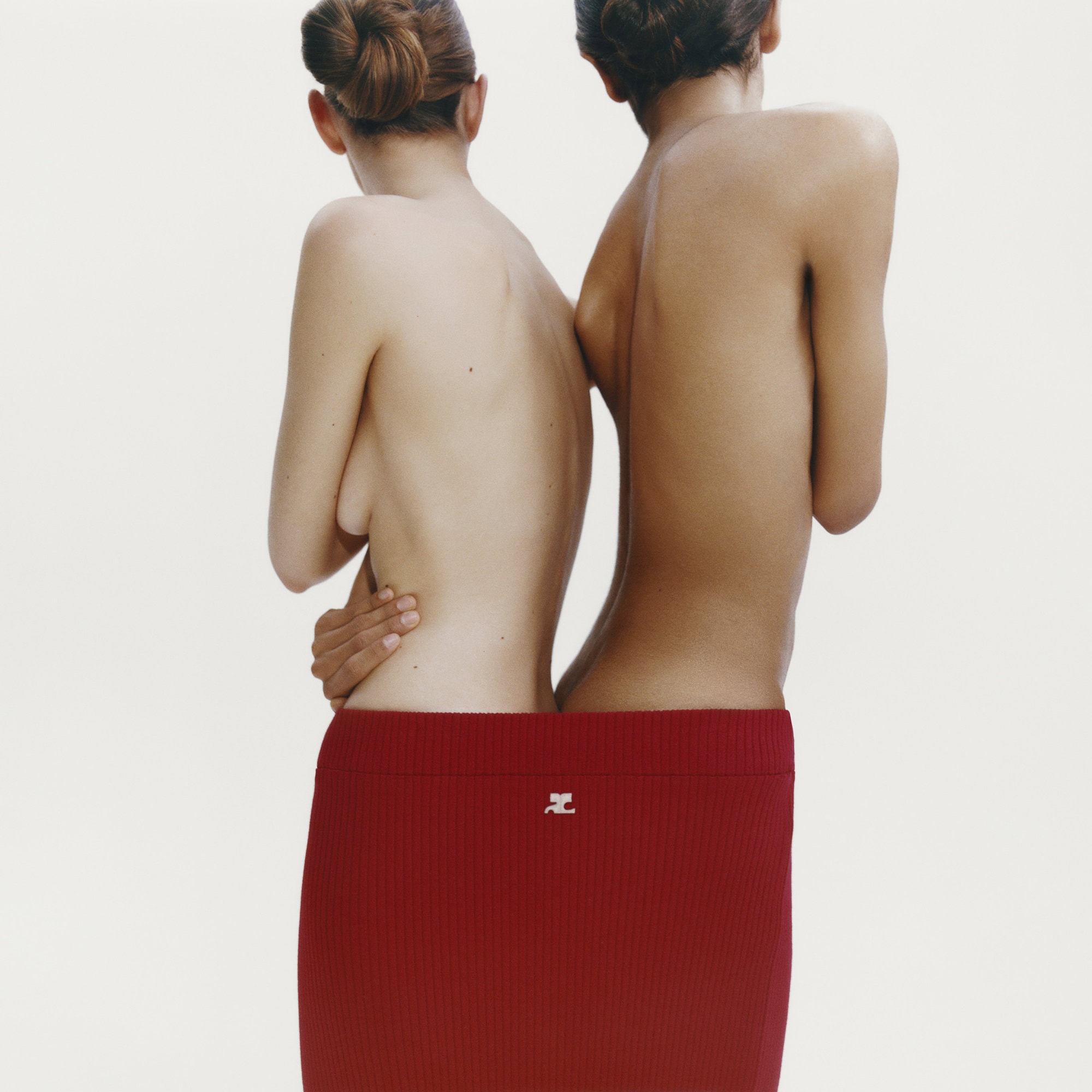 Two women standing back-to-back enclosed together inside a single red ribbed skirt against a plain white background