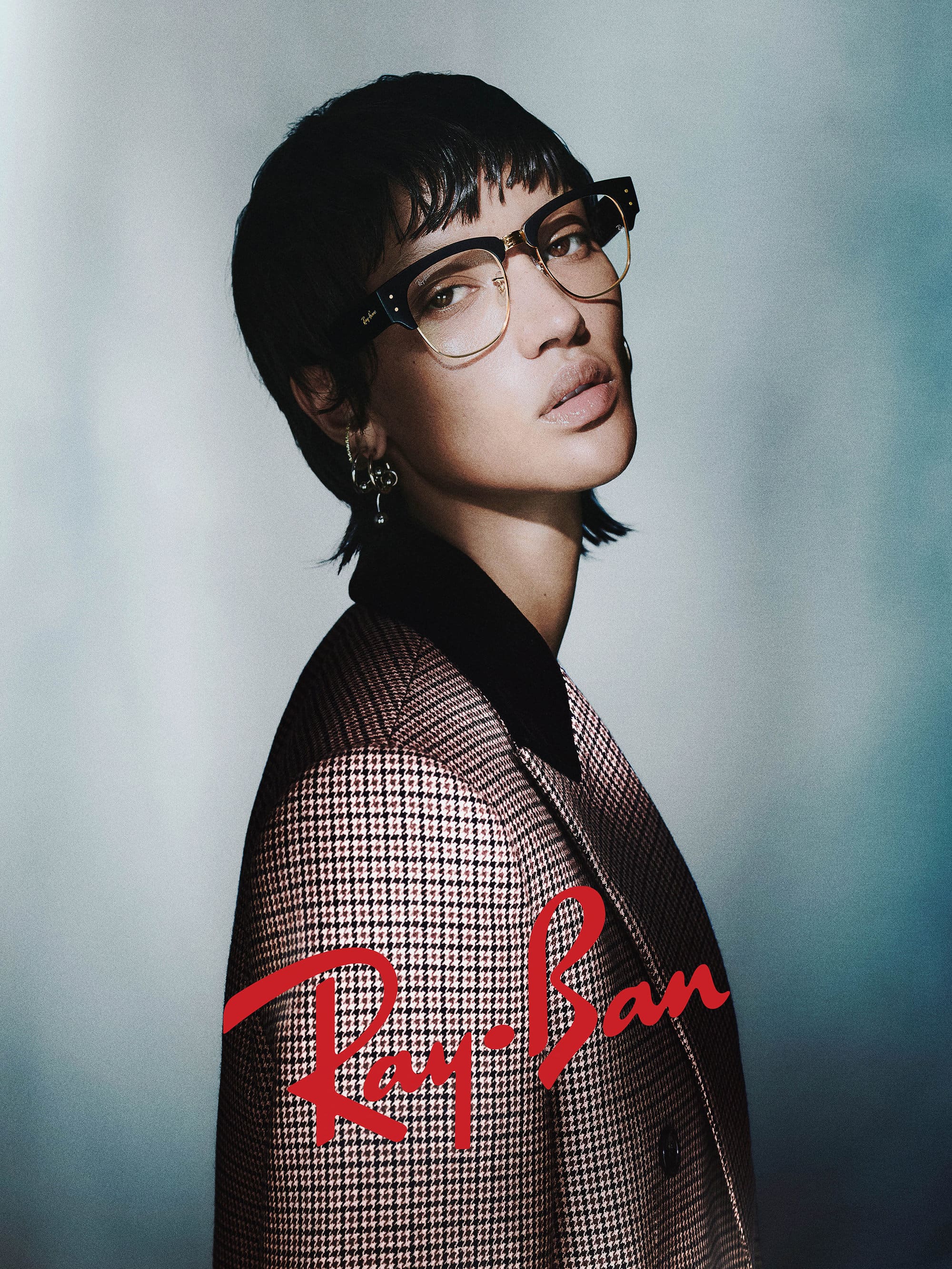 Model wearing eyeglasses and a patterned blazer against a gradient studio background in an ad campaign