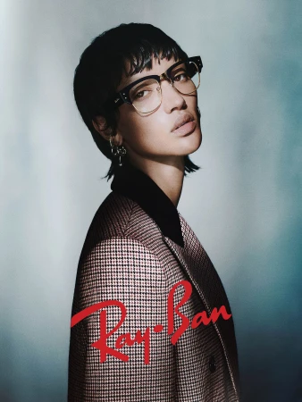 Model wearing eyeglasses and a patterned blazer against a gradient studio background in an ad campaign